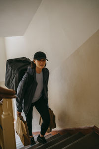 Female delivery person holding parcels and moving up on stairs in building