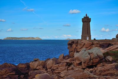 Lighthouse on rock by sea against sky