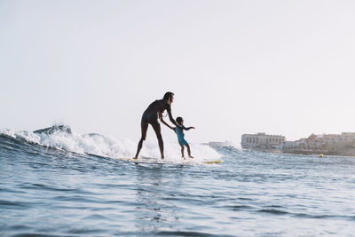 Pulled back view of mother and son surfing a small wave at sea