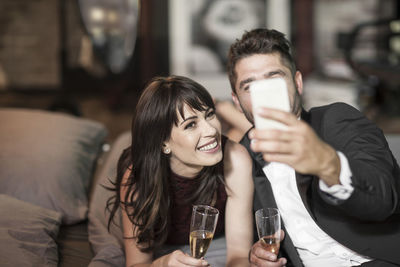 Smiling couple in elegant clothing drinking champagne in bed and taking a selfie