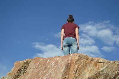 Rear view of woman standing on rock against blue sky