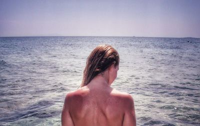 Rear view of shirtless young woman against sea