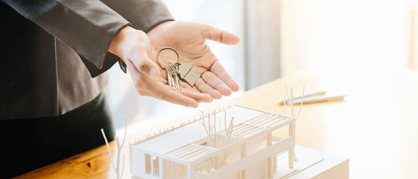 Midsection of real estate agent holding key by model house