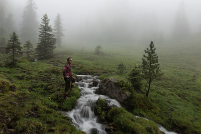 Side view of man standing by stream during foggy weather