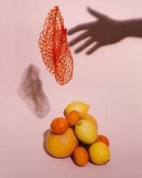 Still life with citrus fruits, orange net floating and the shadow of a hand on a pink background