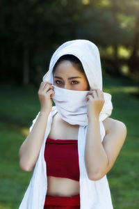 Portrait of young woman covering face with scarf while standing on field