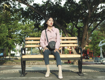 Portrait of young woman sitting on bench in park