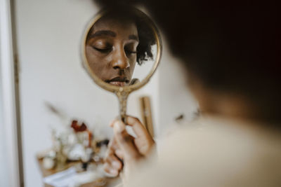 Woman holding mirror with eyes closed at home