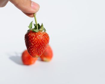 Close-up of hand holding strawberry over white background