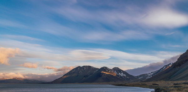 Scenic view of sea by mountains against sky during sunset