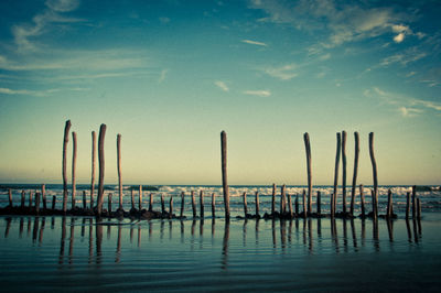 Silhouette wooden posts in sea against sky