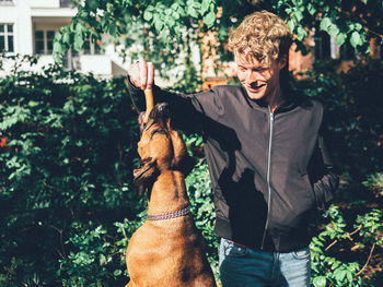 Smiling young man feeding sausage to dog in yard