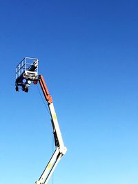 Low angle view of cherry picker against clear blue sky