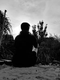 Rear view of man sitting on field against sky