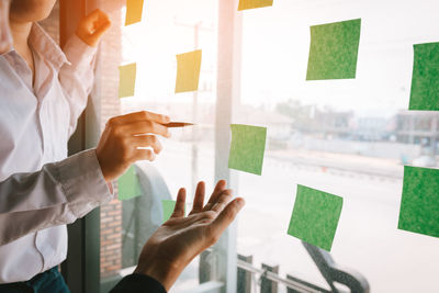 Midsection of colleagues gesturing towards adhesive notes on glass wall