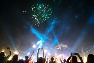 People enjoying concert against firework display at night