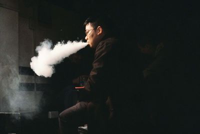 Man exhaling smoke while sitting in darkroom