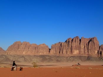 Woman sitting against rock formations and clear blue sky