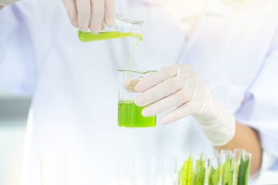Midsection of scientist pouring green liquid into measuring beaker