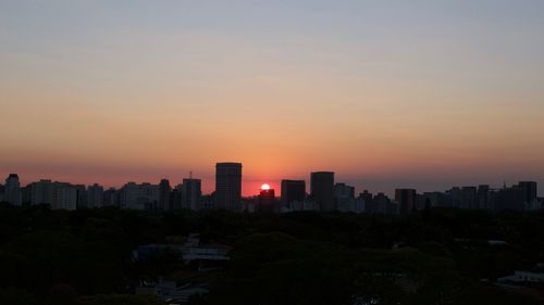 Silhouette buildings in city against sky during sunset