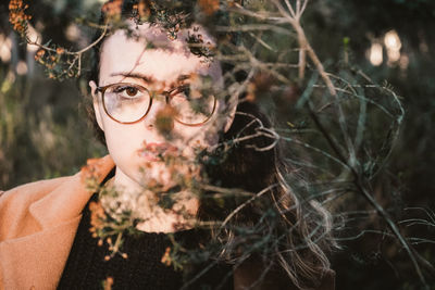 Close-up portrait of young woman wearing eyeglasses by plants in park