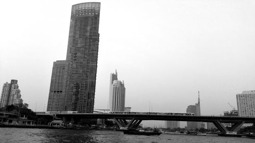 Bridge over river by buildings against clear sky