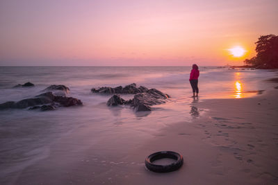 Full length of woman standing at beach against sky during sunset