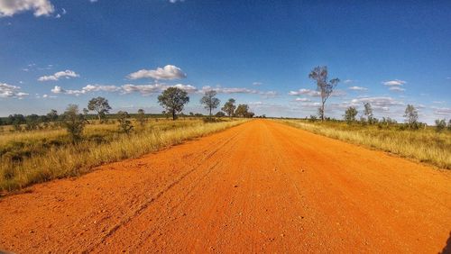 Dirt road amidst field against sky