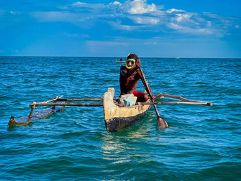 Rear view of man kayaking in sea against sky