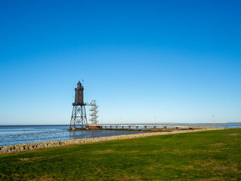 Lighthouse by sea against clear blue sky