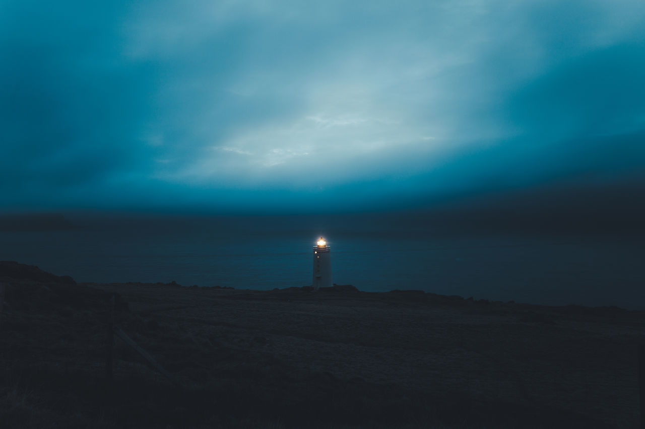 Illuminated lighthouse by sea against sky at night