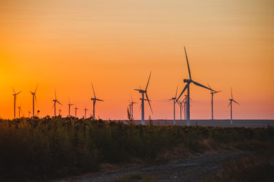 Windmills on field against sky during sunset