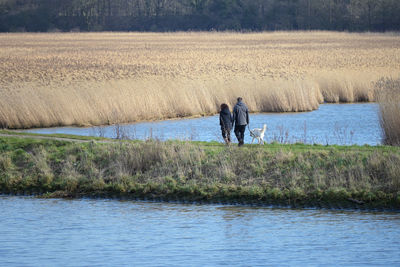 Rear view of men standing on field by lake