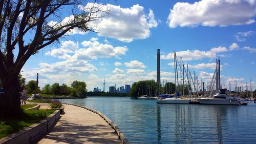 Boats moored at harbor by river against sky