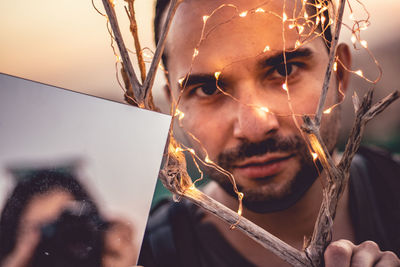 Close-up portrait of man with illuminate lights and mirror during sunset