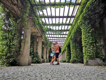 Side view of young couple standing by plants and columns in park