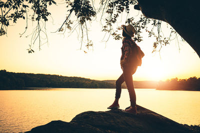 Silhouette woman standing by lake against sky during sunset