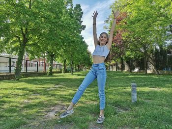 Full length portrait of happy girl standing on grass against trees