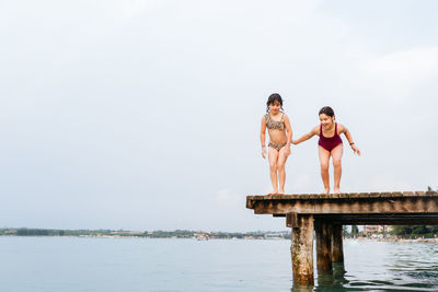 Two children jumping from the pier  in the water