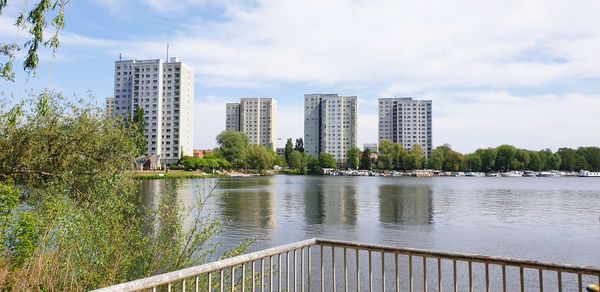 Modern buildings by river against sky in city