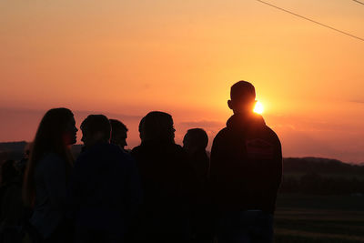 Silhouette people against orange sky during sunset