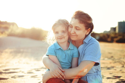 Mother embracing daughter sitting on beach