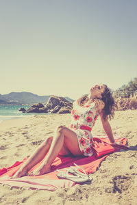 Portrait of woman sitting on sand at beach against clear sky