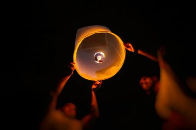 People holding lit candle against black background
