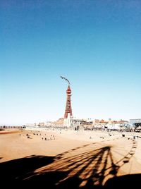 Shadow of ferris wheel at beach in city against clear blue sky