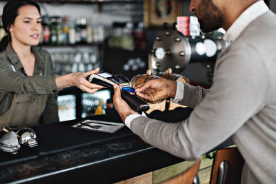 Midsection of customer doing credit card payment to female owner at checkout counter