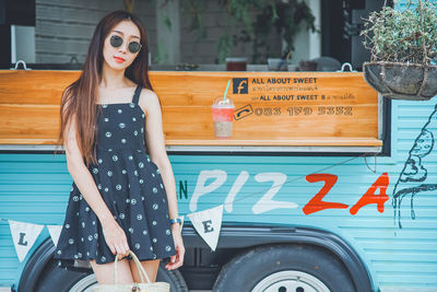 Young woman wearing sunglasses standing against food truck