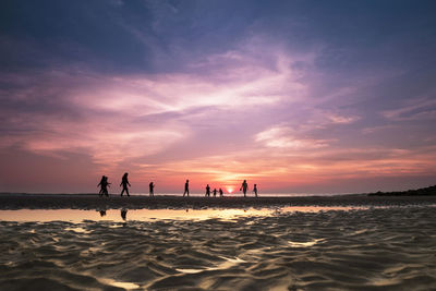 Silhouette people at beach against sky during sunset