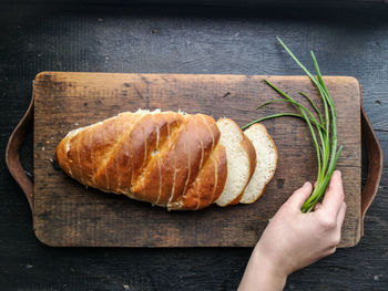 Cropped hand of person chives by bread on cutting board
