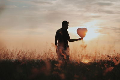 Full length of man holding balloon on field at sunset